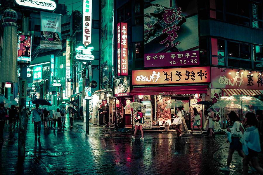 People walk down the street in Tokyo, Japan, at night with colorful street signs lit up.